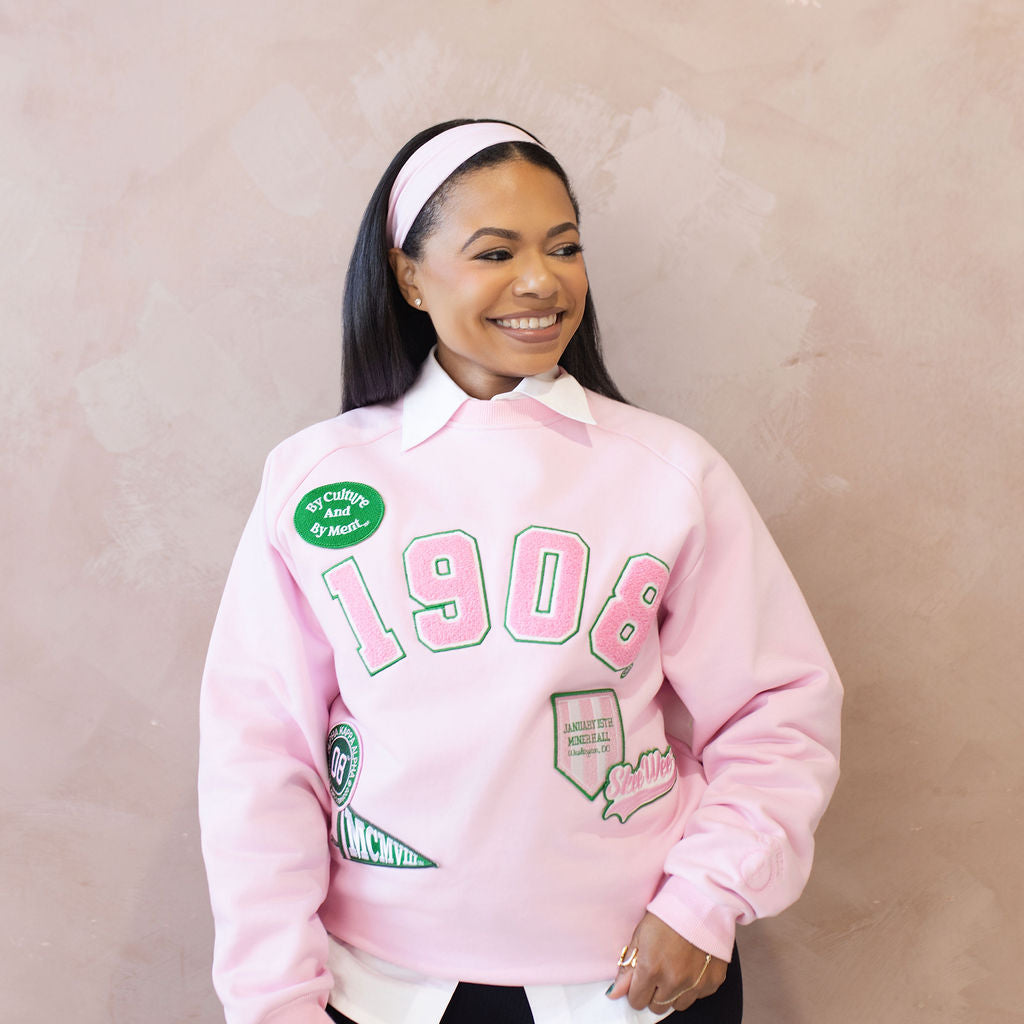 Person wearing a pink sweatshirt with text and embroidered patches on a beige background