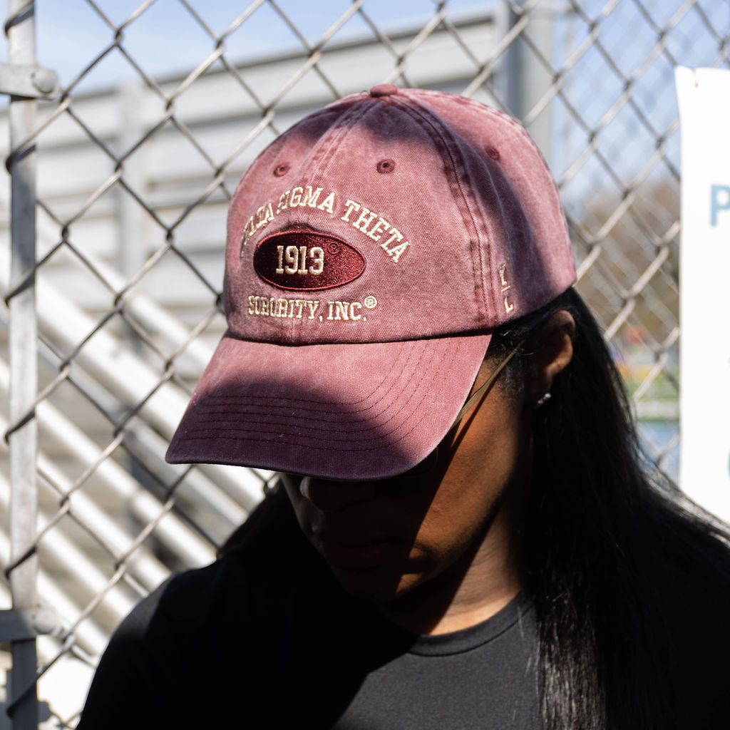 Person wearing a maroon baseball cap with text in front of a chain-link fence.