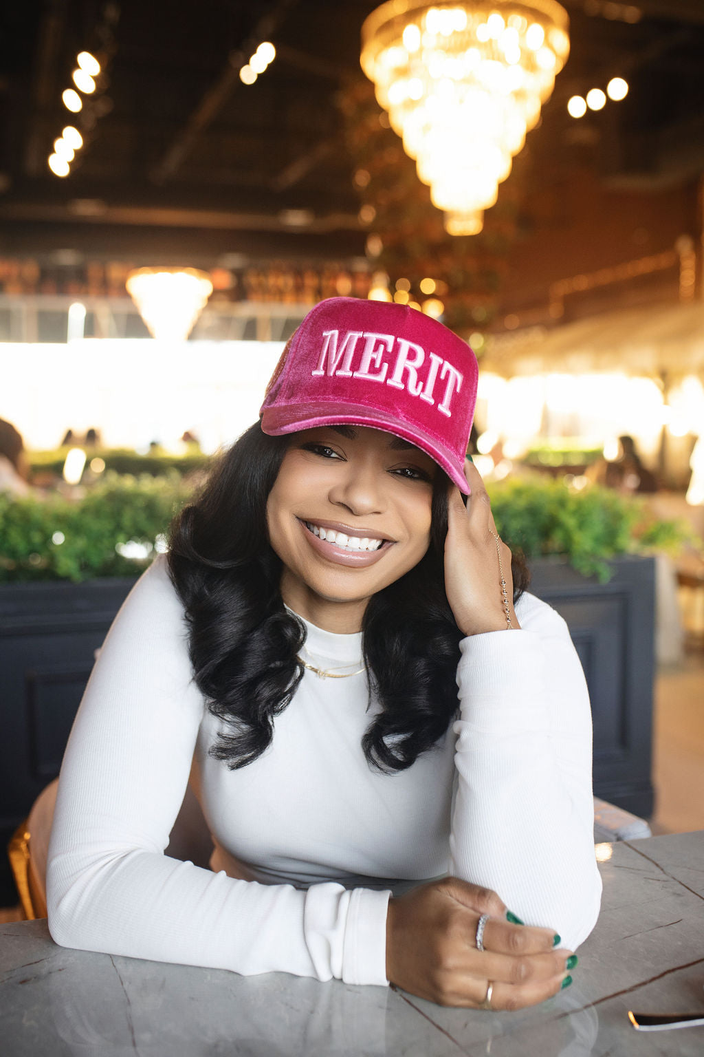 Woman wearing a pink 'MERIT' cap in a restaurant setting
