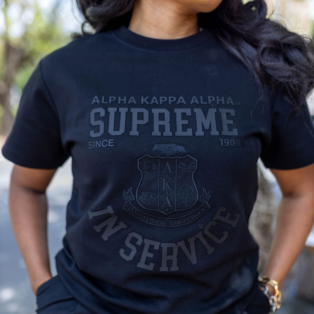 Person wearing a black 'Alpha Kappa Alpha Supreme' t-shirt with a logo.