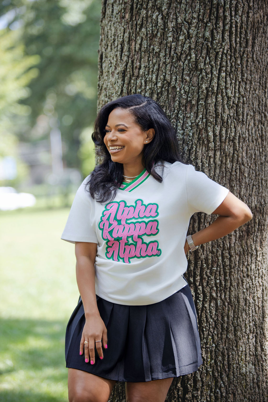 Woman wearing a white t-shirt with 'Alpha Kappa Alpha' text, standing next to a tree outdoors.