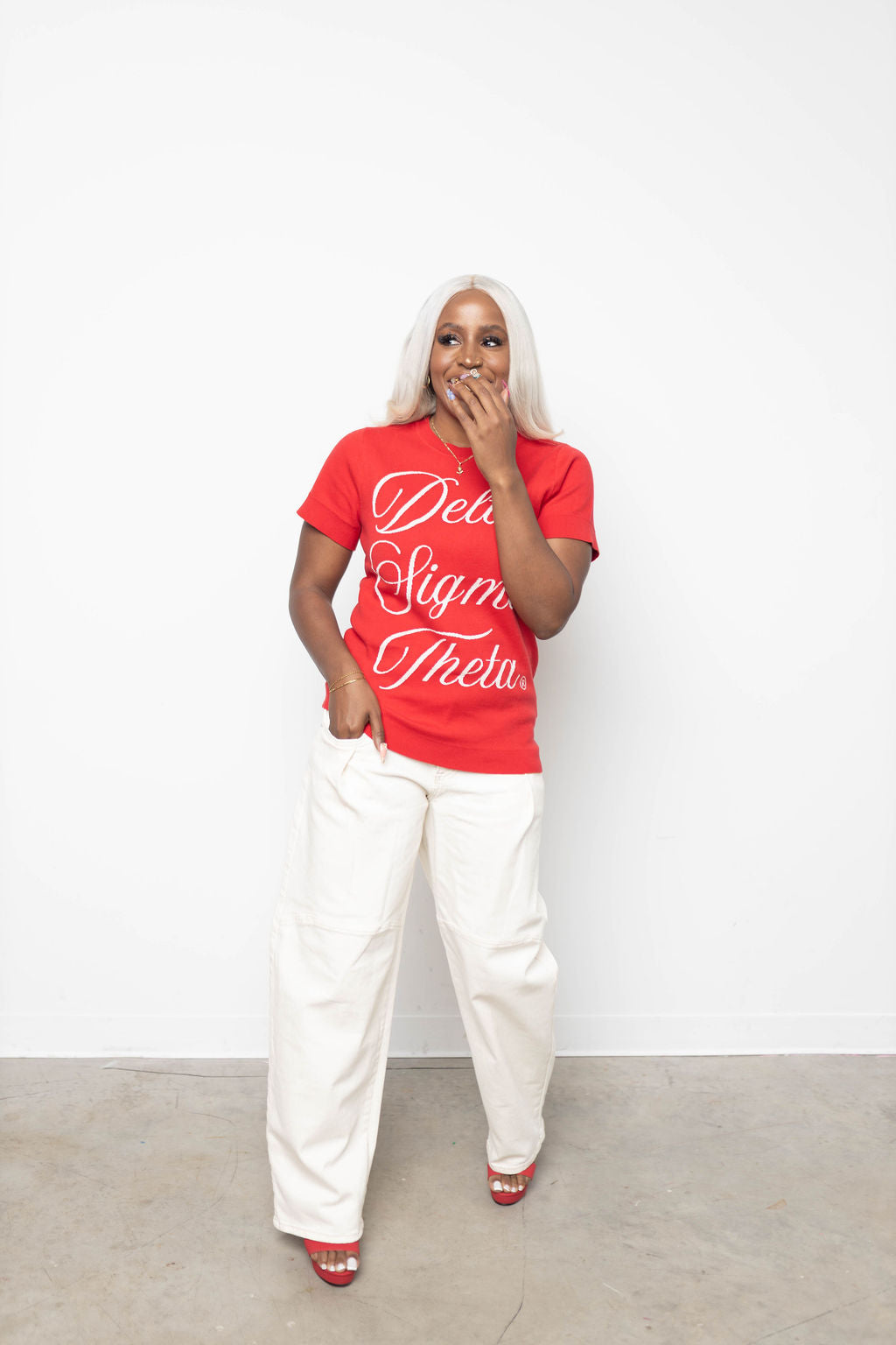 Person wearing a red knit with white text and white pants against a white background