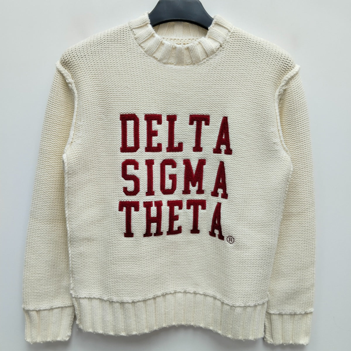 White sweater with 'Delta Sigma Theta' text on a hanger against a light gray background