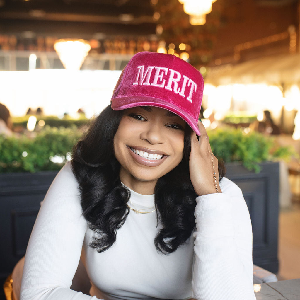 Woman wearing a pink 'MERIT' cap in a restaurant setting