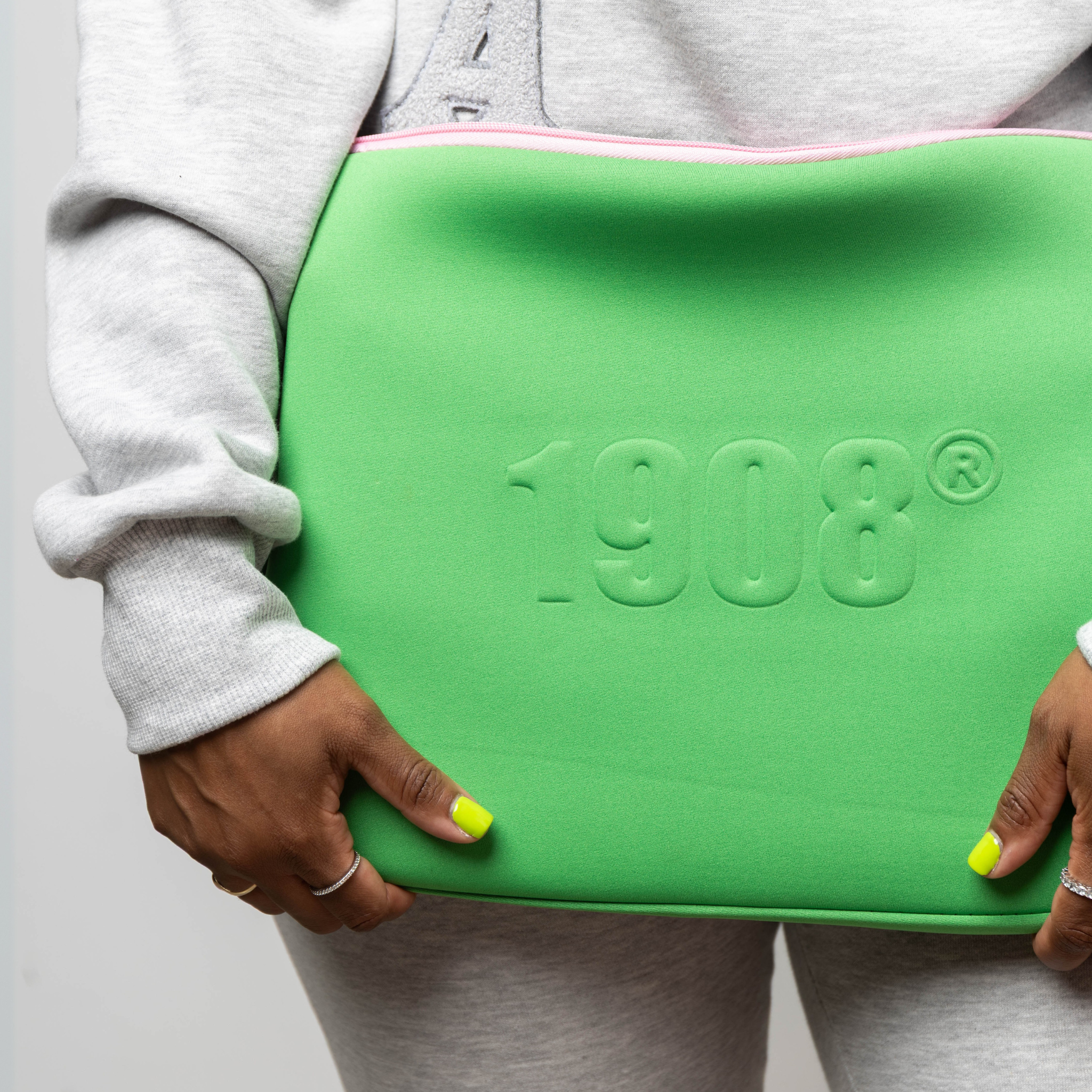 Person holding a green laptop sleeve with '1908' embossed branding on a plain background