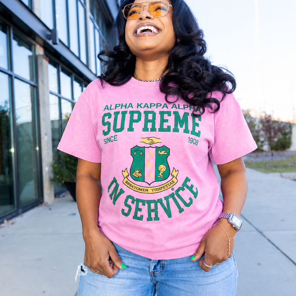 Person wearing a pink t-shirt with green text and graphics, standing outdoors.