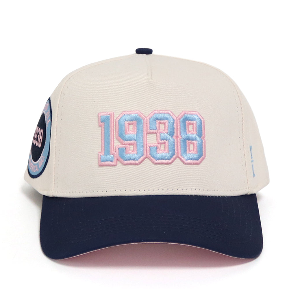 Cream and navy cap with '1938' embroidery with a pink outline on a cream background