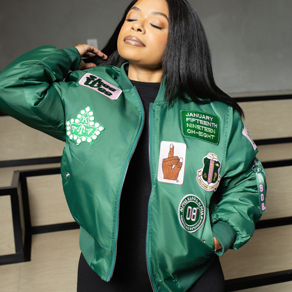 Person wearing a green jacket with various patches against a neutral background