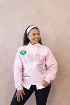 Person wearing a pink sweatshirt with text and embroidered patches on a beige background