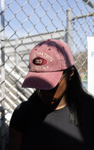 Person wearing a maroon baseball cap with text in front of a chain-link fence.
