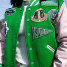 Person wearing a green letterman jacket with patches outdoors