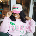 Person wearing a pink sweatshirt with '1908' and a cap with 'MERIT' text