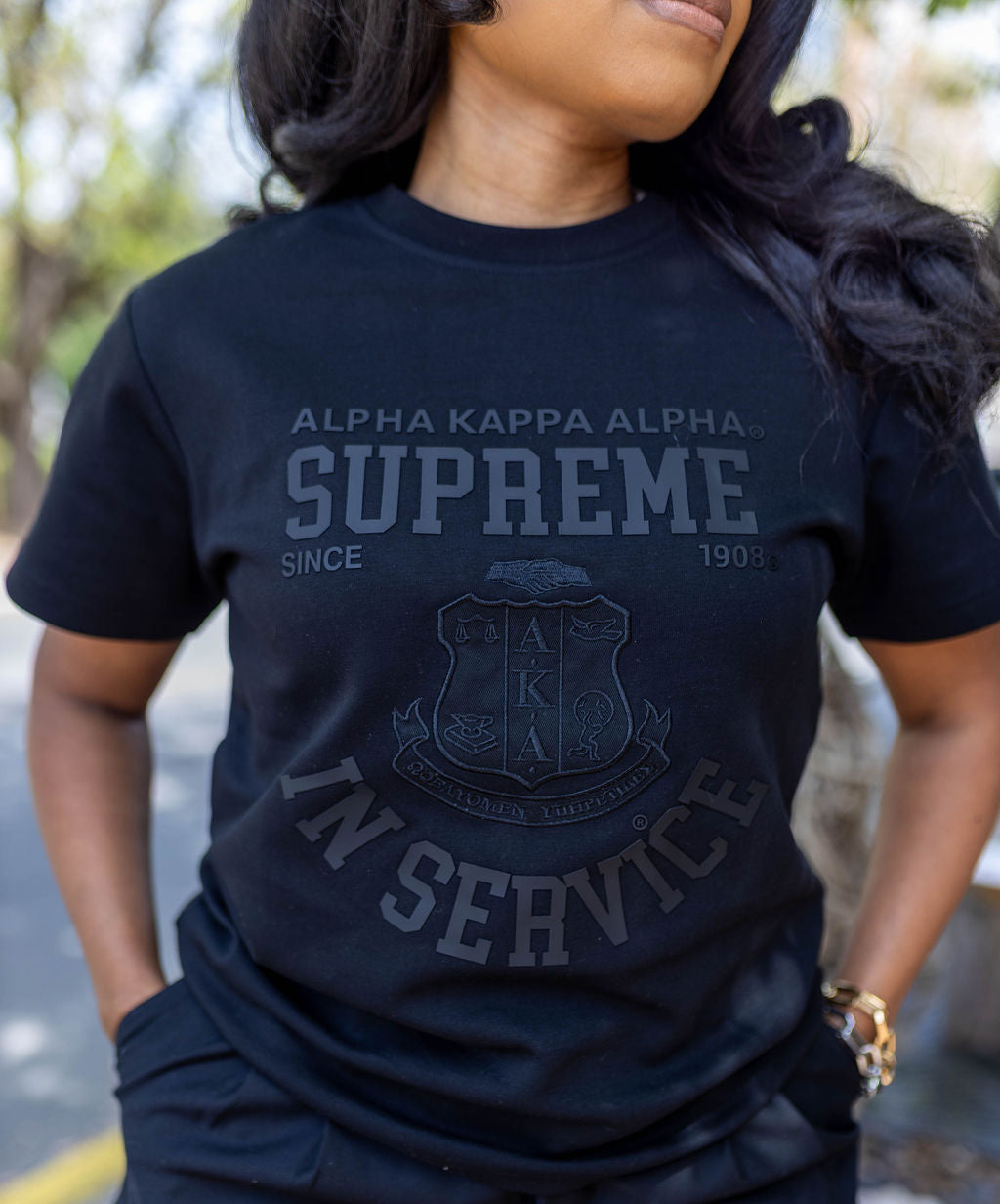 Person wearing a black 'Alpha Kappa Alpha Supreme' t-shirt with a logo.