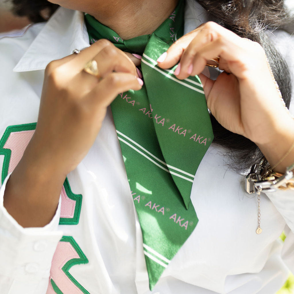 Person wearing a green scarf with 'AKA' text, adjusting it around their neck.