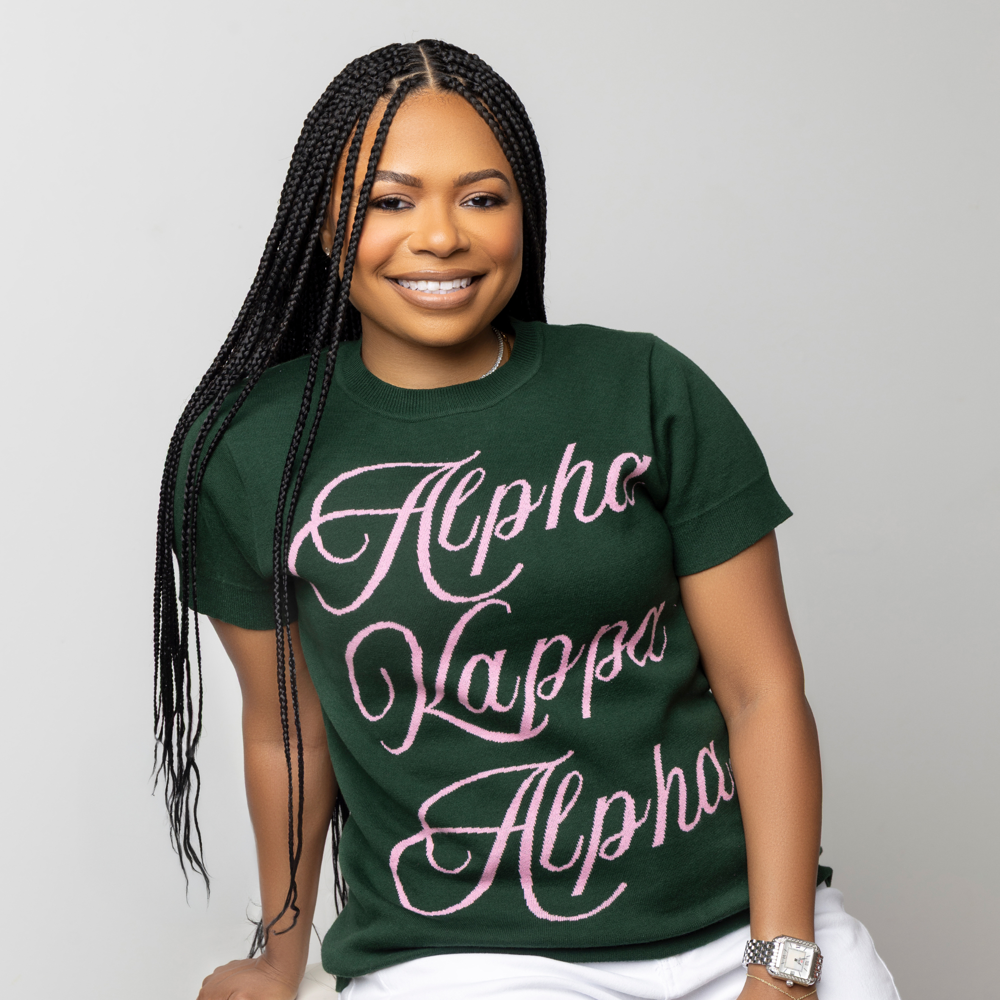 Person wearing a green knit short sleeved sweater with 'Alpha Kappa Alpha' text in pink.