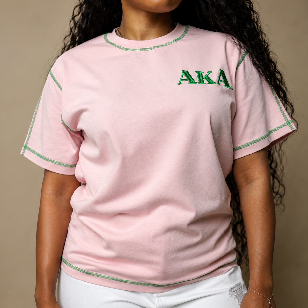Person wearing a pink t-shirt with 'AKA' text on a beige background