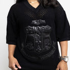 Woman wearing a black textured sweater with a logo on a white background