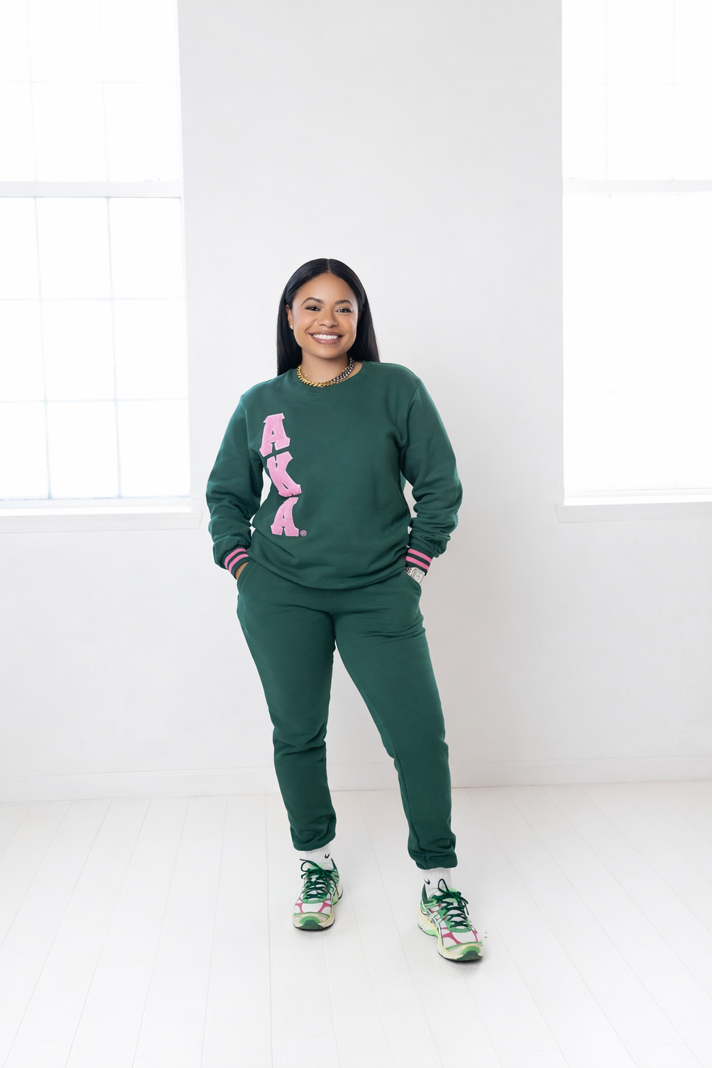 Person wearing a green sweatshirt with pink text and matching pants on a white background