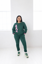 Person wearing a green sweatshirt with pink text and matching pants on a white background