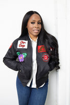 Woman wearing a black bomber jacket with patches against a white background