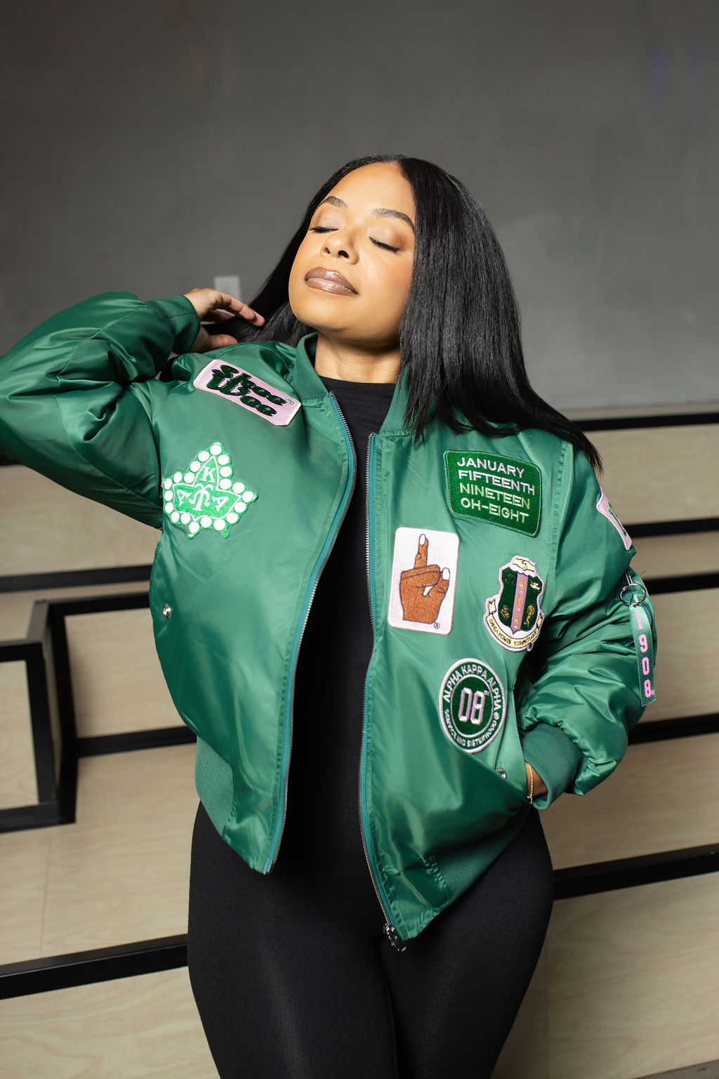 Person wearing a green jacket with various patches against a neutral background