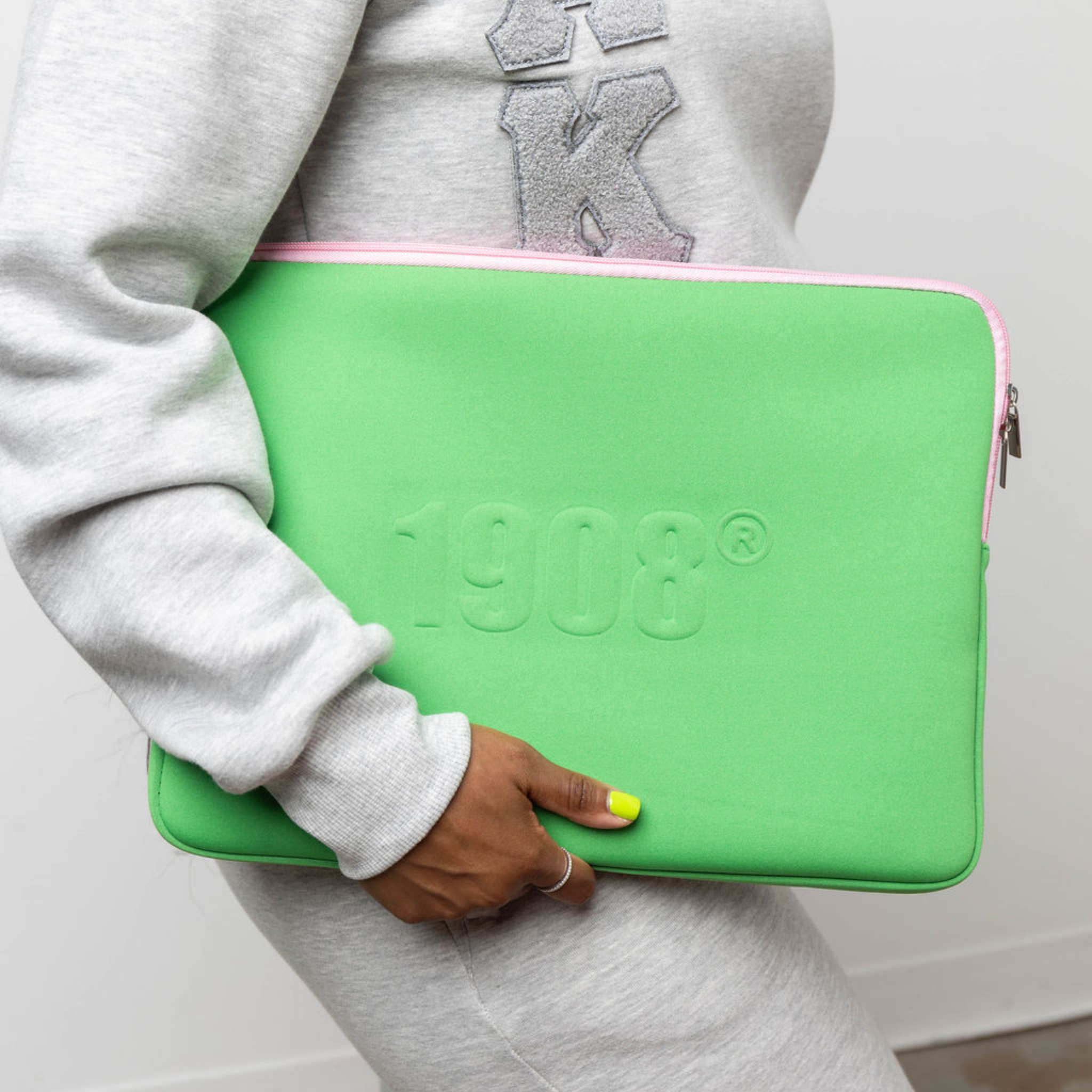 Person holding a green laptop sleeve with '1908' branding.